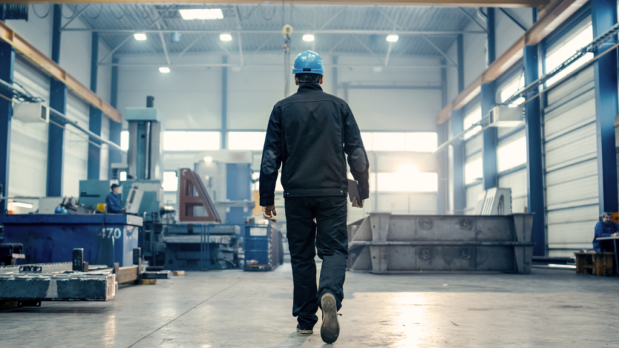 Man in safety helmet walking in an industrial space, representing the role of safety mats in preventing workplace accidents