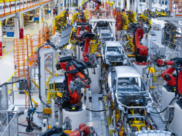 A wide shot of an automotive production line with robotic arms and workers wearing high-visibility safety vests and helmets showcasing machine safety. This conveys a professional, tech-driven manufacturing environment.