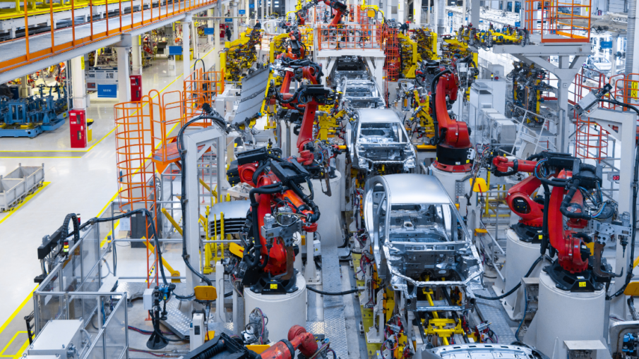 A wide shot of an automotive production line with robotic arms and workers wearing high-visibility safety vests and helmets showcasing machine safety. This conveys a professional, tech-driven manufacturing environment.