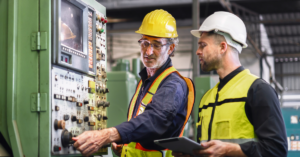 Experienced worker training a new employee on machine safety protocols, demonstrating the proper use of safety devices in an industrial setting.