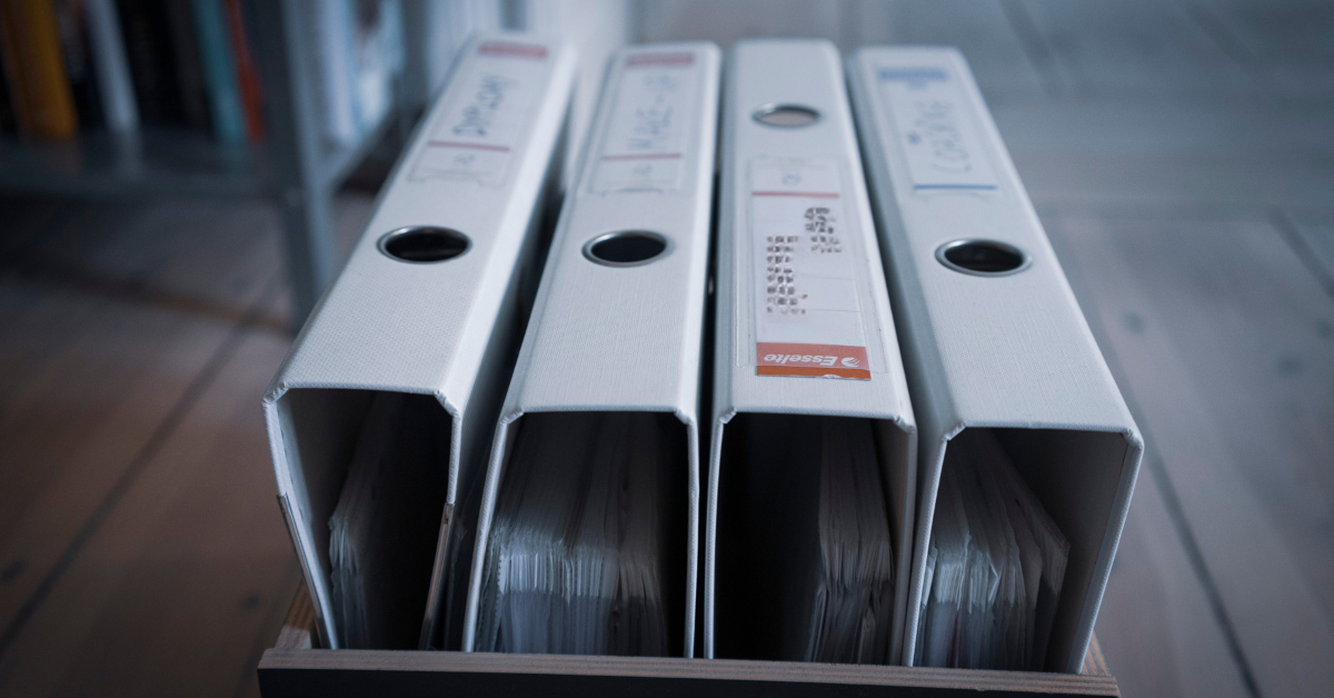 Stack of binders filled with safety compliance documents, regulations, and guidelines for maintaining workplace safety and machine guarding standards.
